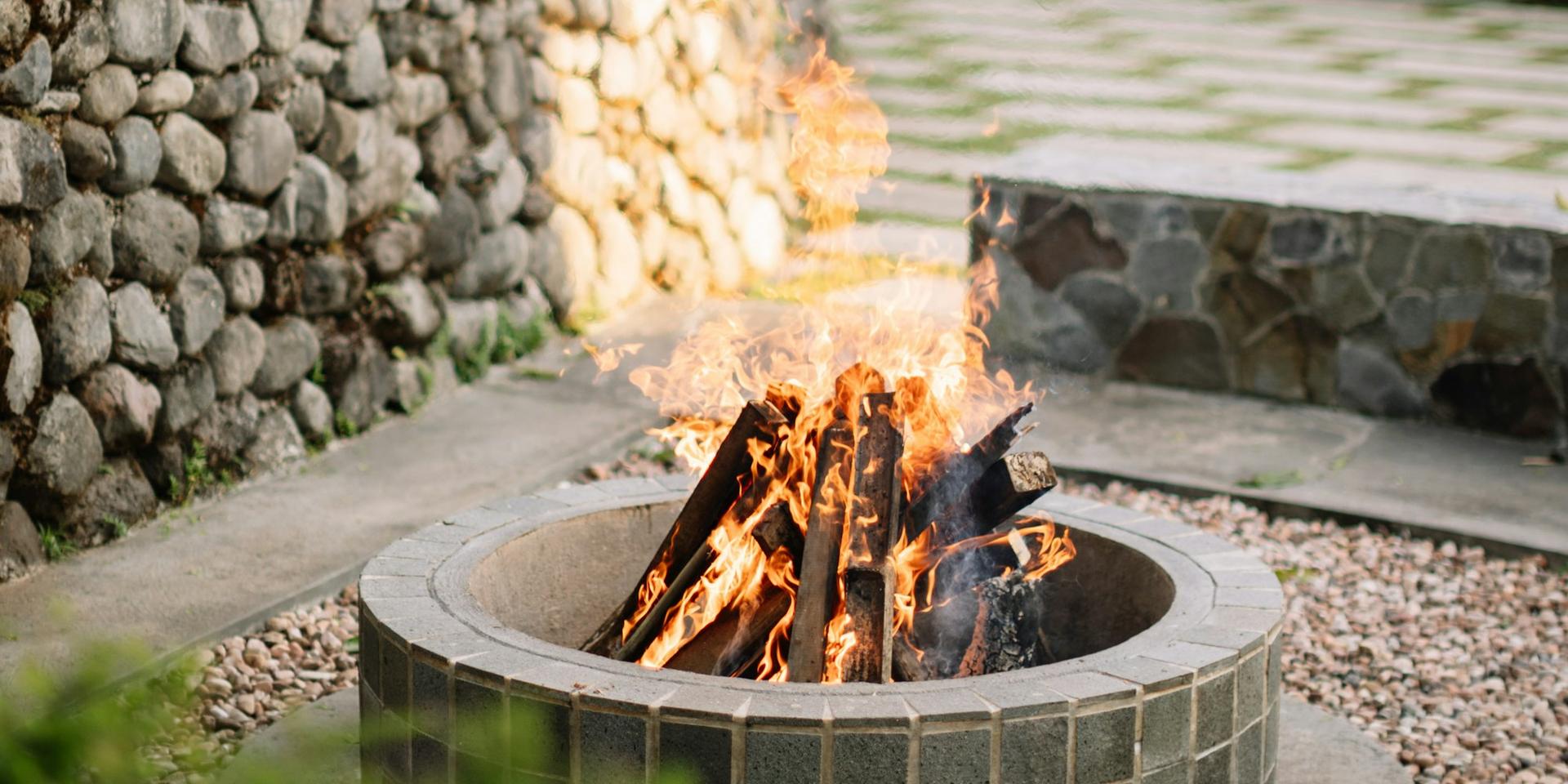 A stone fire pit burning at the edge of a patio
