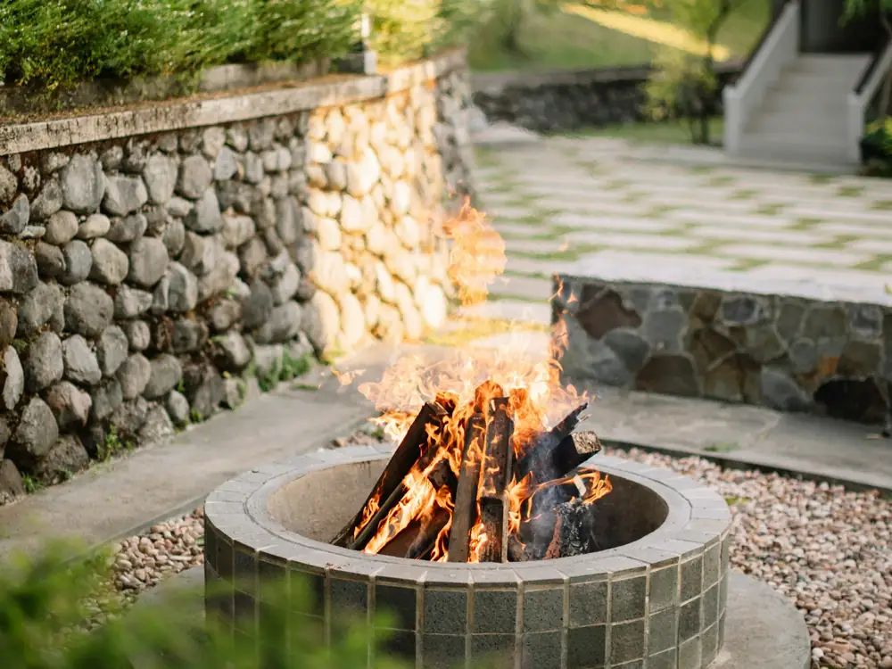 Round stone fire pit burning beside a fieldstone wall