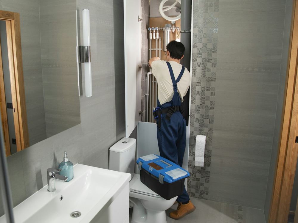 Plumber with a toolbox in a small bathroom (illustrative photo)