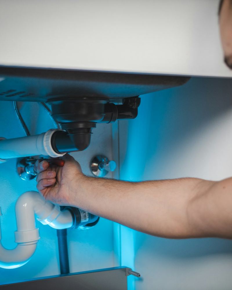 Hands loosening a sink trap under a vanity (illustrative photo)