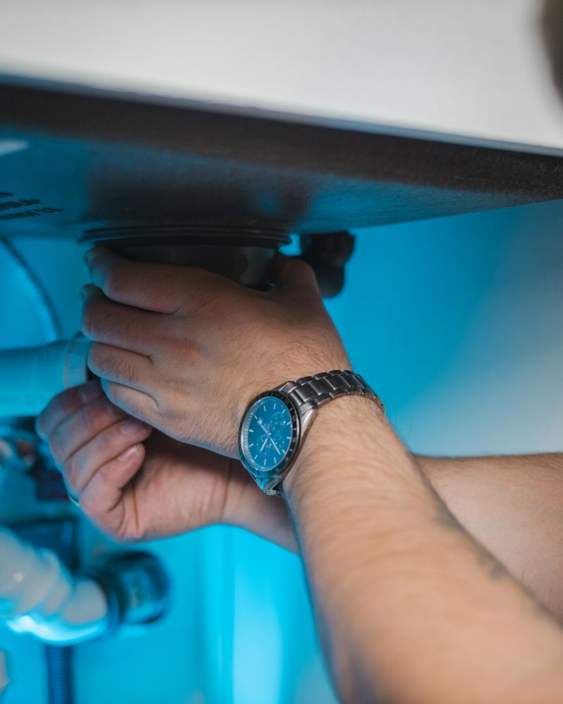 Plumber tightening a fitting under a sink (illustrative photo)