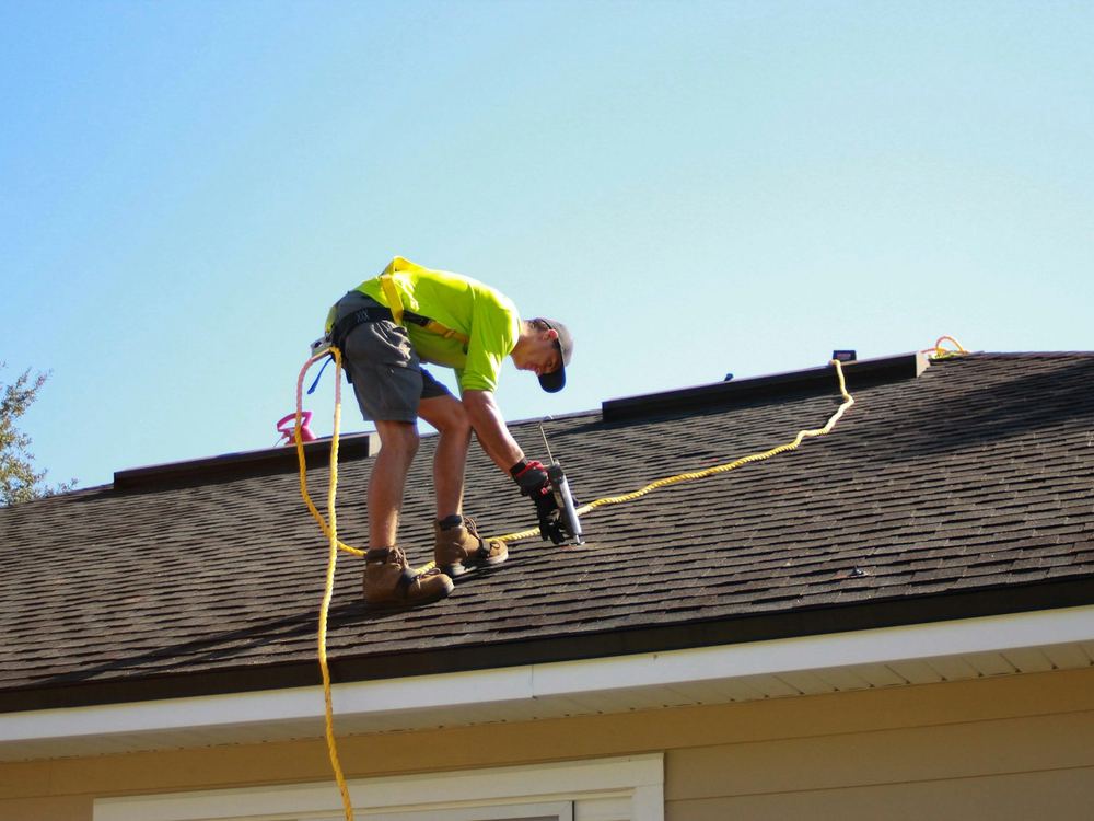Roofer nailing architectural shingles (illustrative photo)