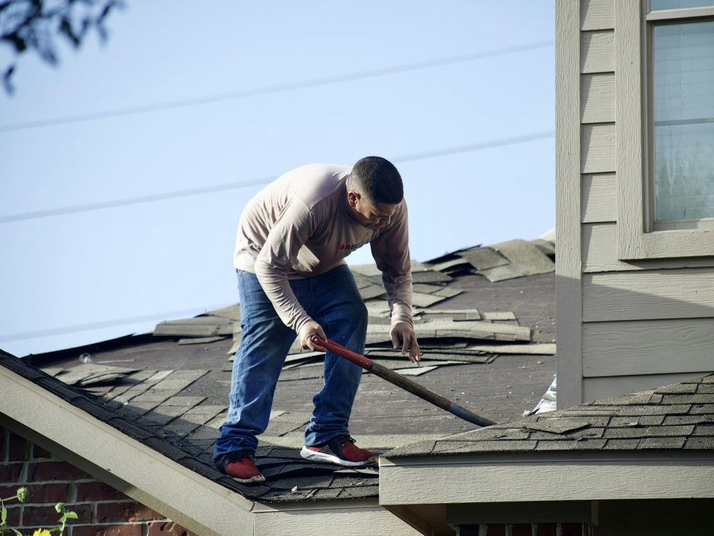 Roofer clearing storm-damaged shingles (illustrative photo)